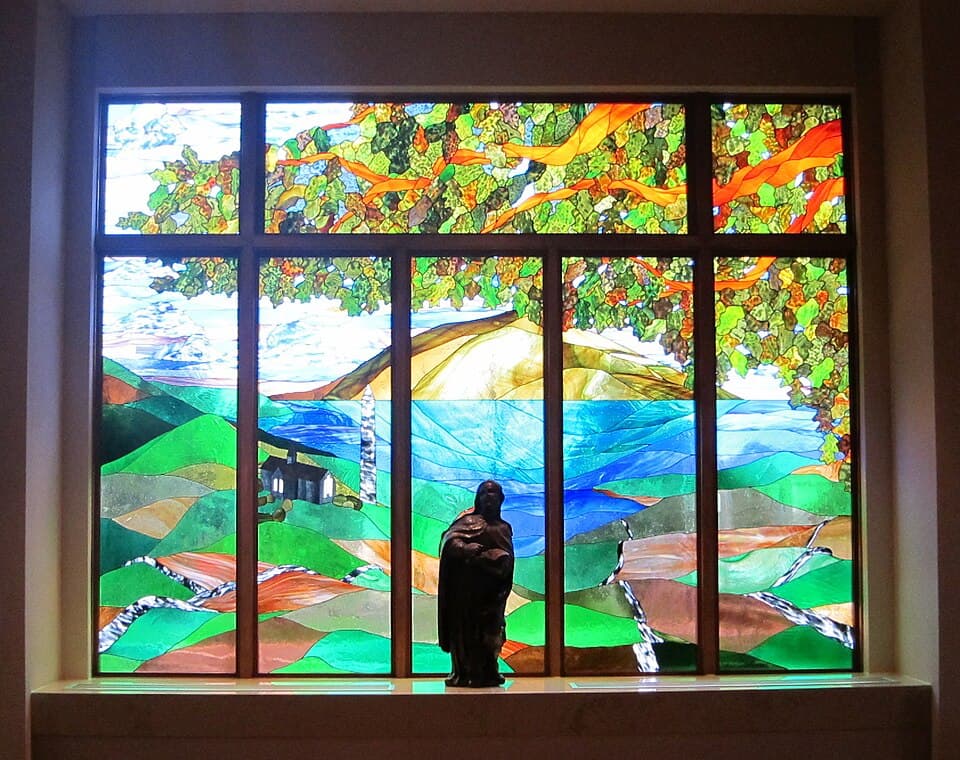 St. Brigid of Kildare - statue of Saint Brigid in front of stained glass landscape