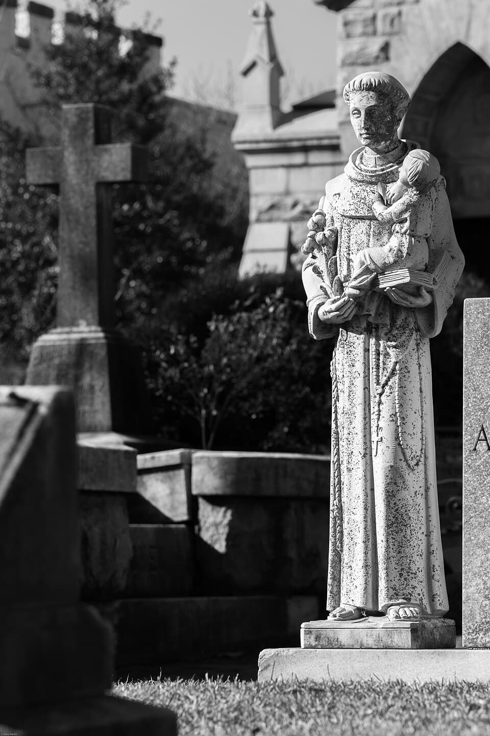Statue of friar with flowers, bible and babe in arms at Oakland Cemetery